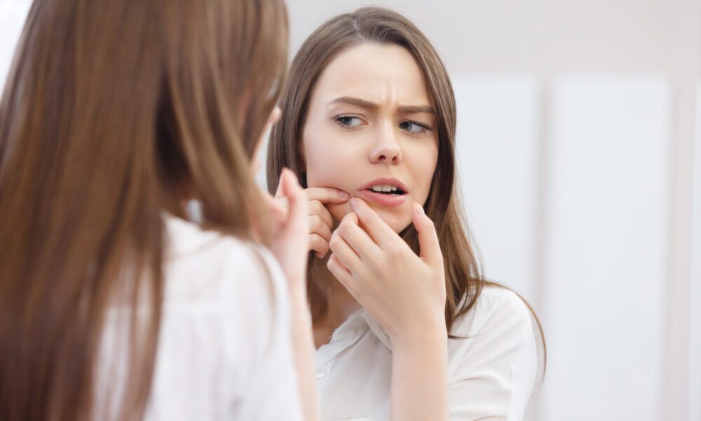 Mulher apertando espinha no queixo e olhando no espelho